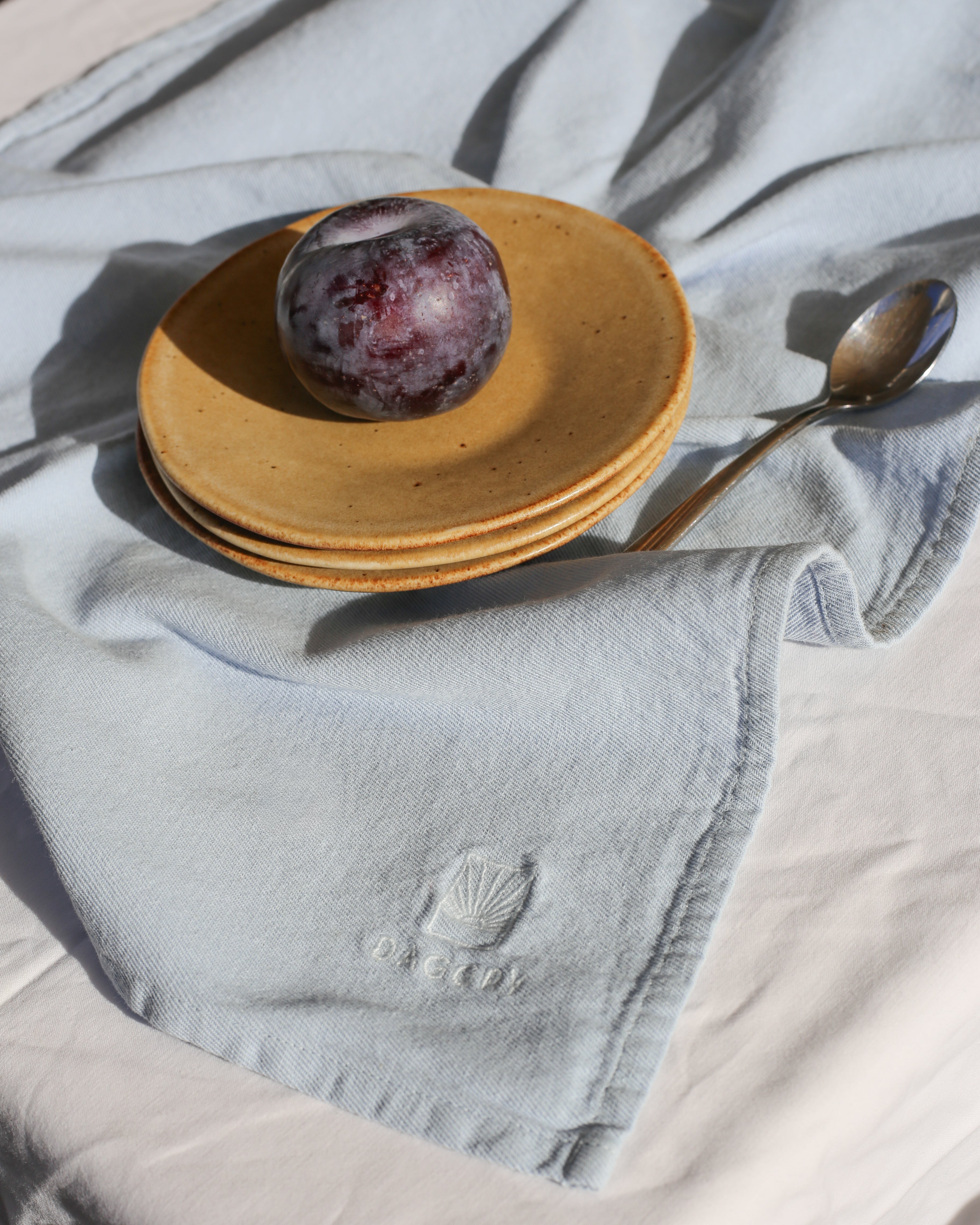 Plum on a stack of yellow ceramic plates with a spoon on a light blue fabric background