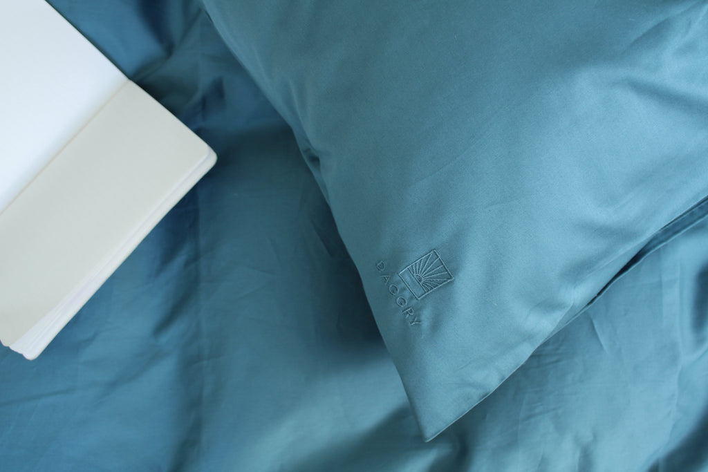 Teal comforter with a brand logo on a bed