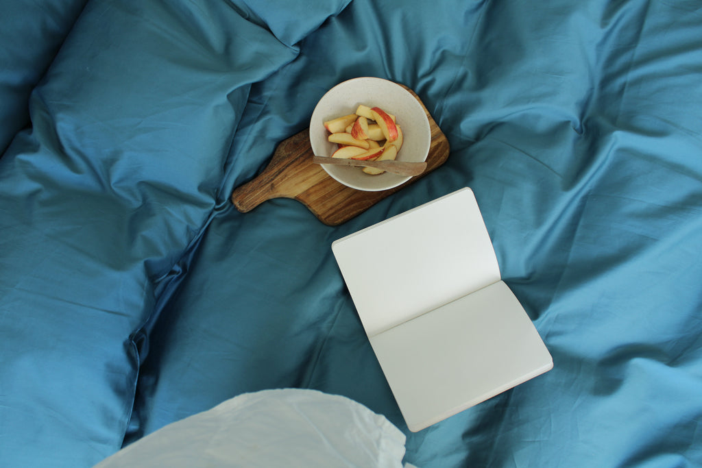 Open book and bowl of fruit on a blue bedspread
