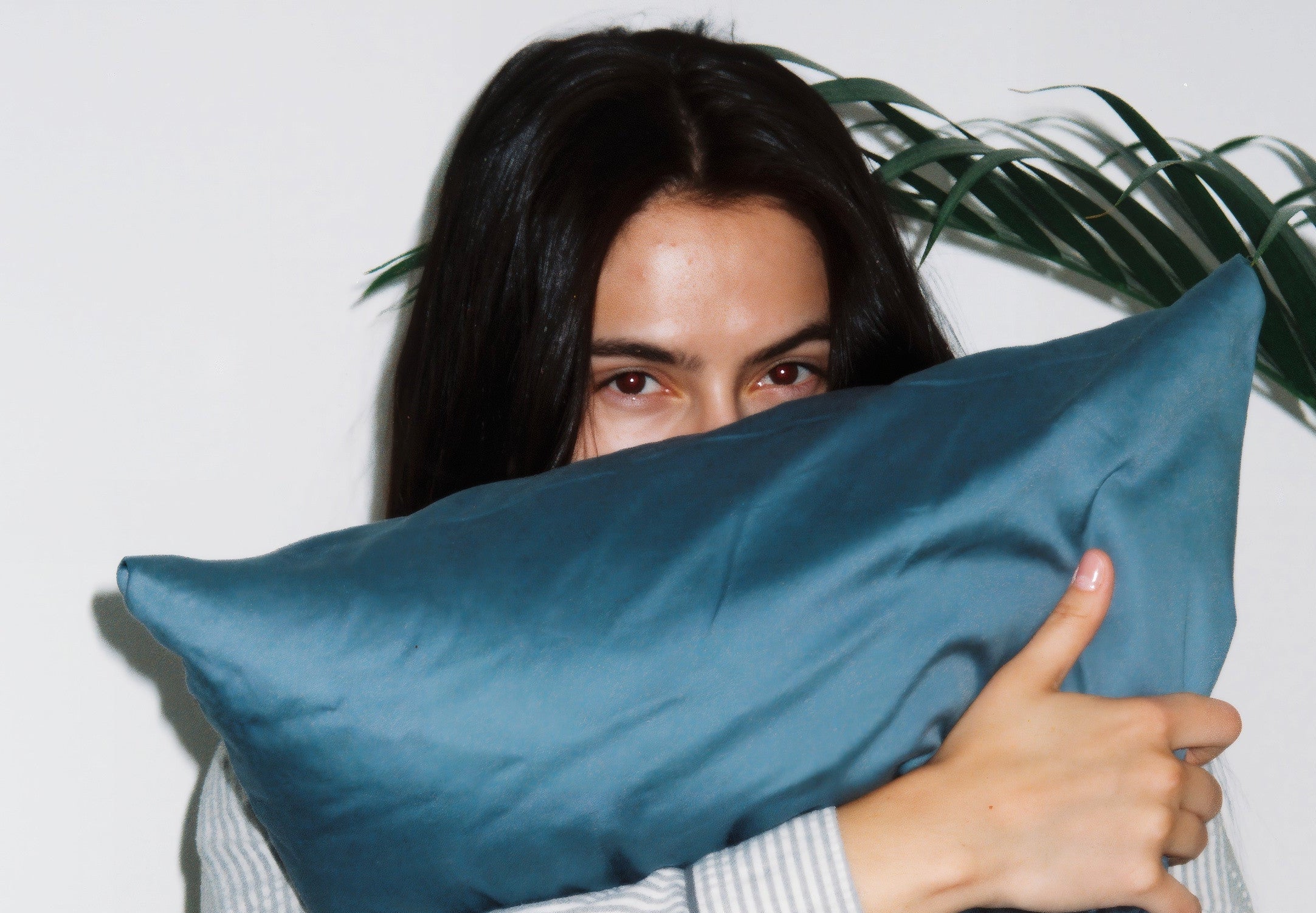 Woman holding a large blue satin pillow against a white background