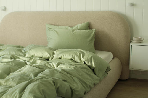Bed with green bedding and pillows against a beige headboard in a room.
