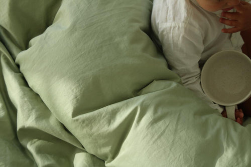 Person lying in bed with green bedding holding a white bowl.