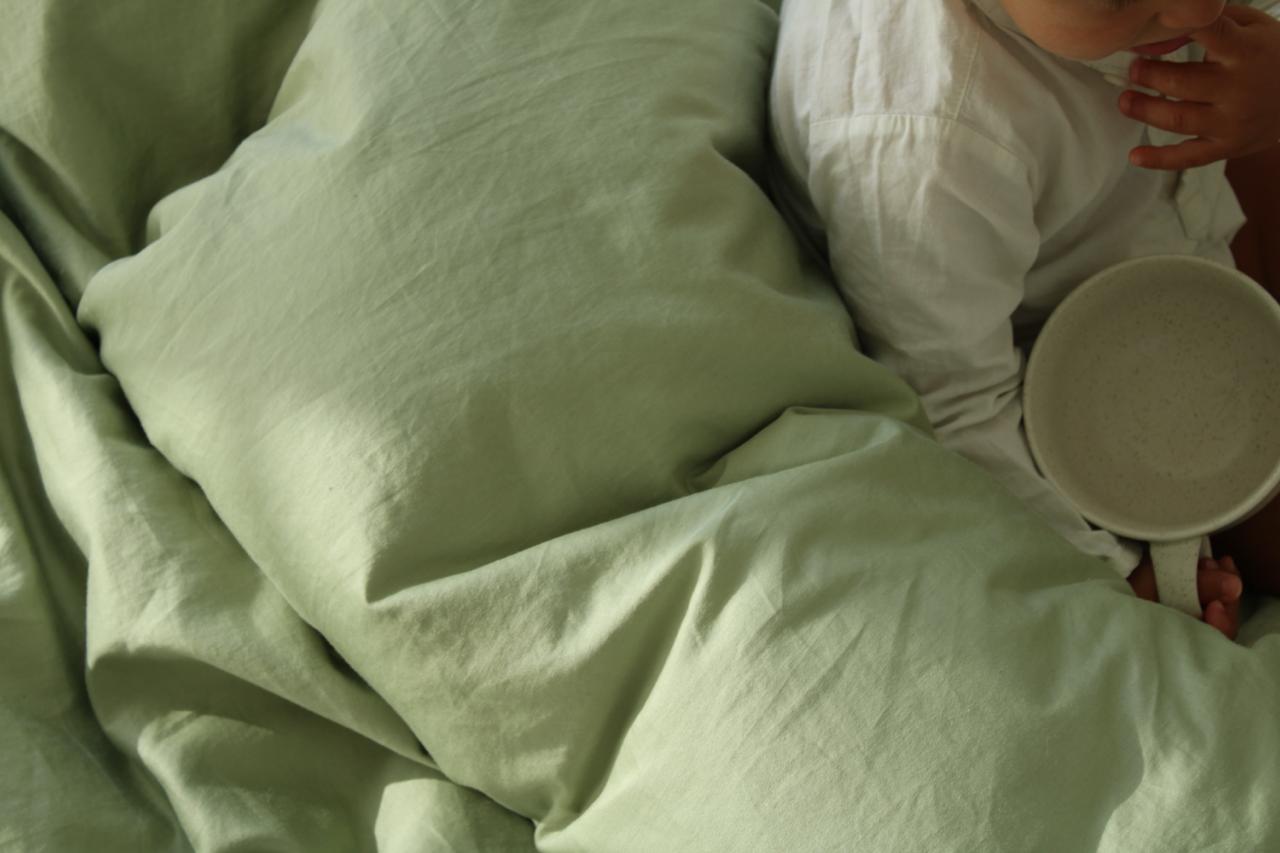 Person lying in bed with green bedding holding a white bowl.