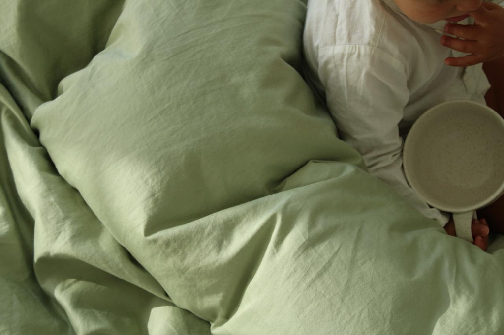 Person lying in bed with green bedding holding a white bowl.
