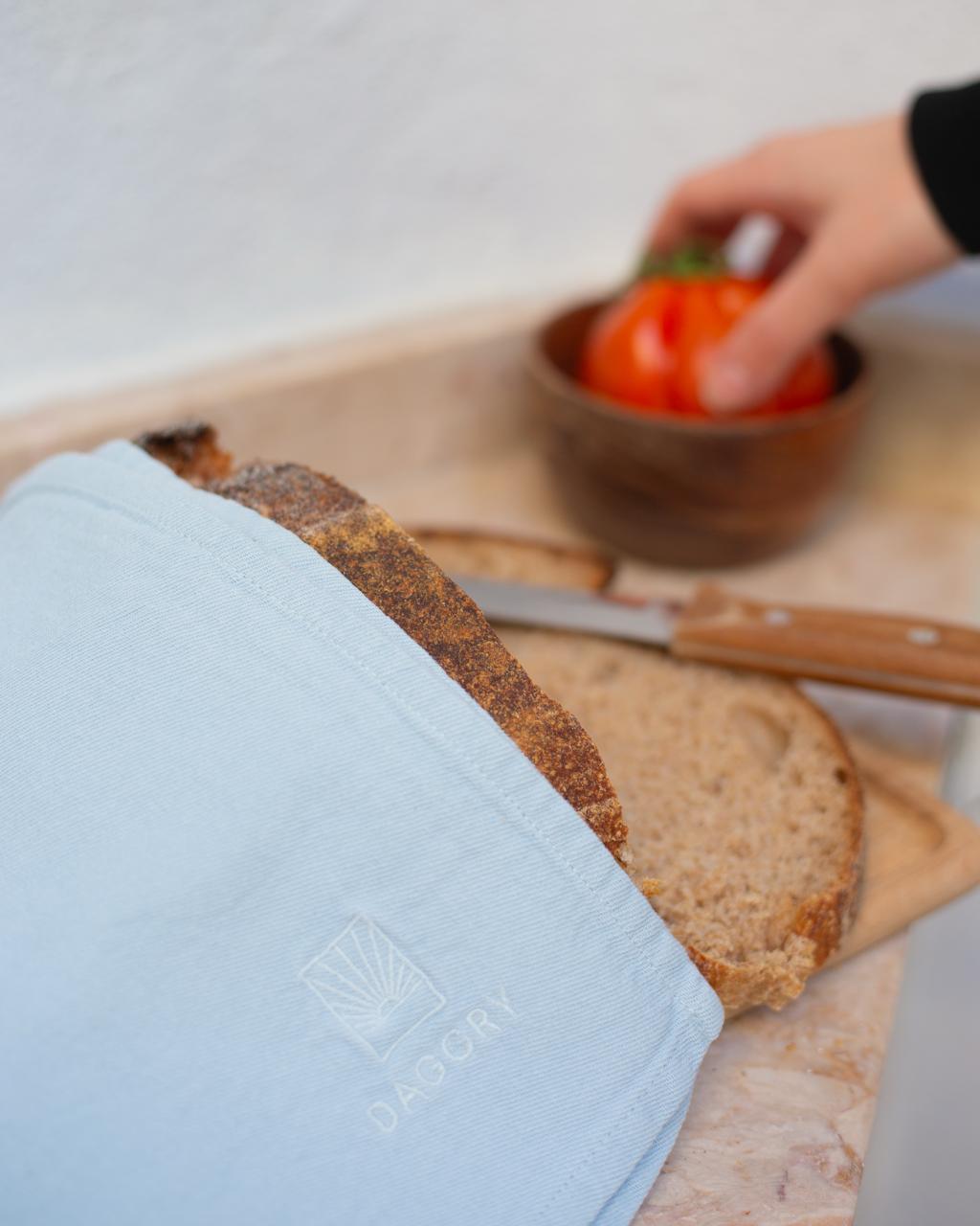 Light blue towel with a brand logo on a wooden cutting board with bread and a knife.