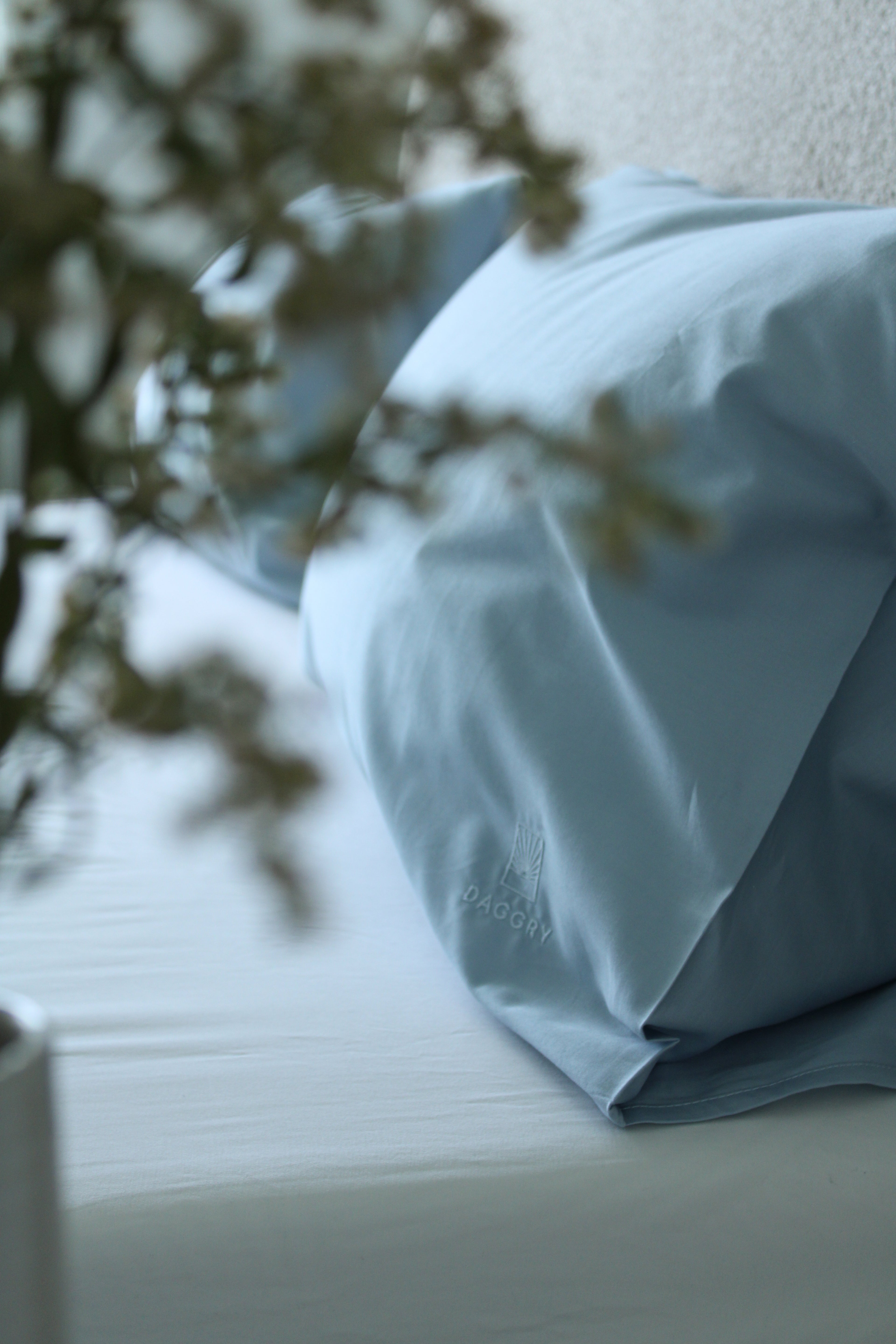 Light blue pillow on a white surface with a blurred plant in the background