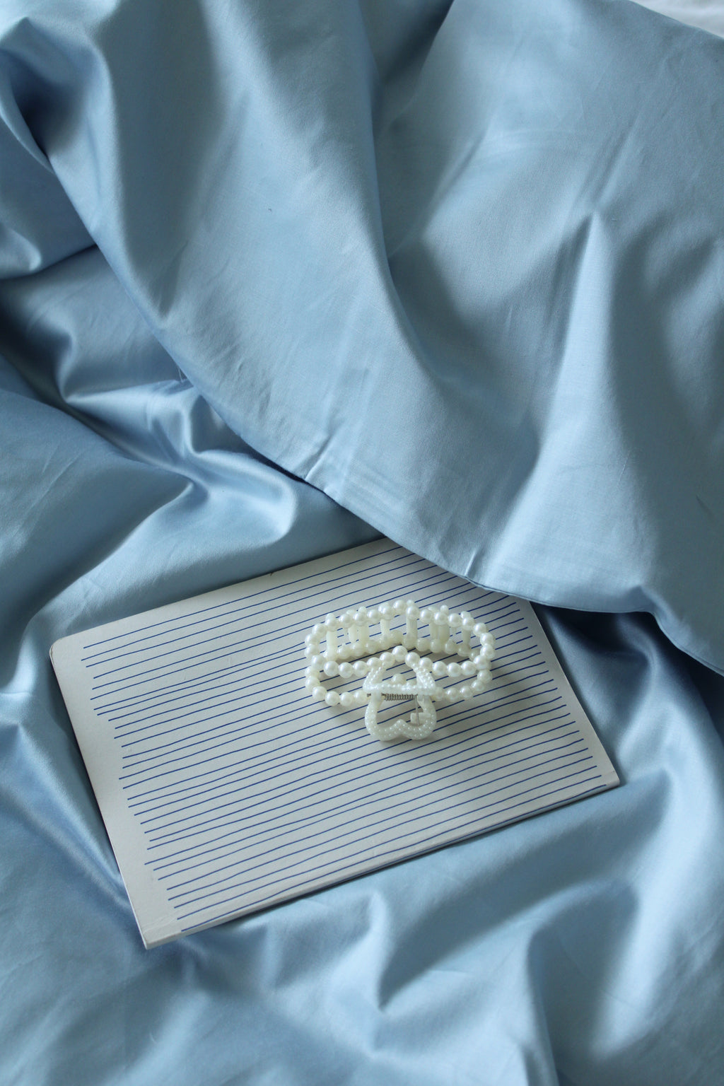 Pearl necklace on a notebook with light blue fabric background