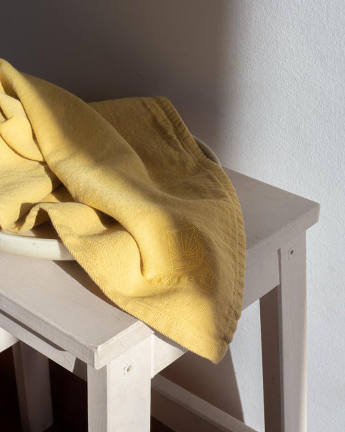 Kjøkkenhåndkle i Mustard over en lys benk.