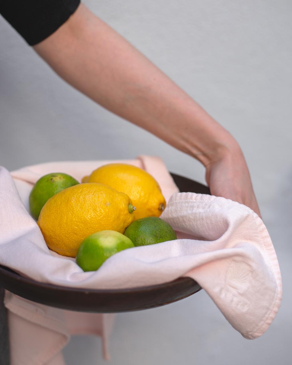 Person holding a bowl of lemons and limes with a white cloth.