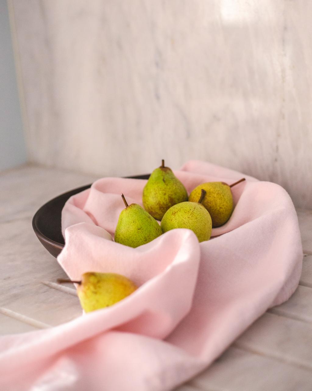 Green pears on a pink cloth with a neutral background