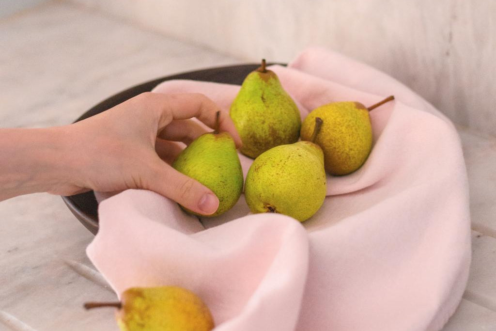 Green pears on a plate held by a person with pink sleeves.
